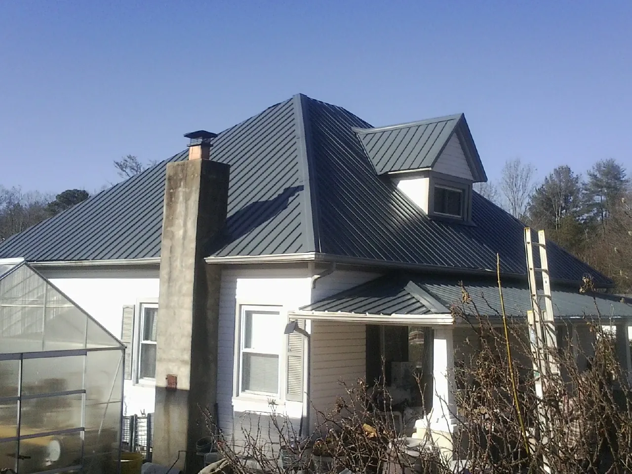 Dark blue standing seam metal roof on a white farmhouse with dormer — Slate & Tile Roof Repair by Roofing Brothers in Youngwood