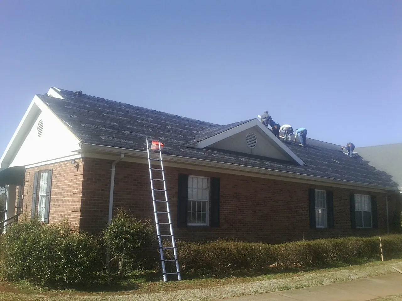 Crew tearing shingles off a brick ranch roof with a ladder set — Metal Roof Repair work by our crew in Youngwood