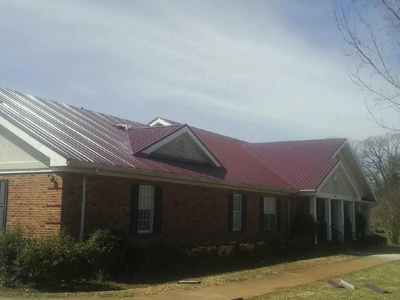 Red metal roof with gabled entries on a long brick building, from a Hail Damage Roof Repair job in Youngwood