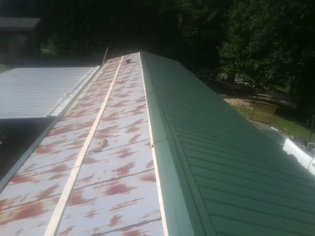 Old rusted panels beside newly installed green metal roofing — Wind Damage Roof Repair by Roofing Brothers in Youngwood