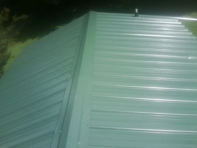 New green metal panels meeting at the ridge of a roof — Flat Roof Repair work by our crew in Youngwood