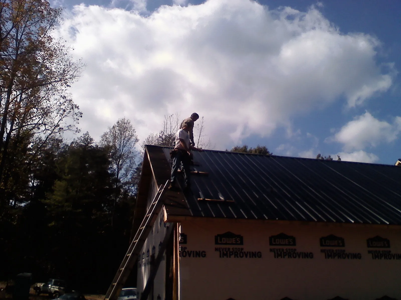 Roofer fastening dark metal panels high against a cloudy sky, from a Roof Inspection job in Youngwood