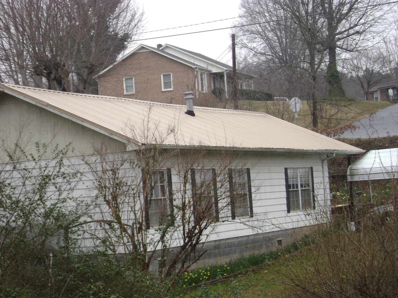 Tan metal roof on a white sided house set into a hillside — Commercial Roofing by Roofing Brothers in Youngwood