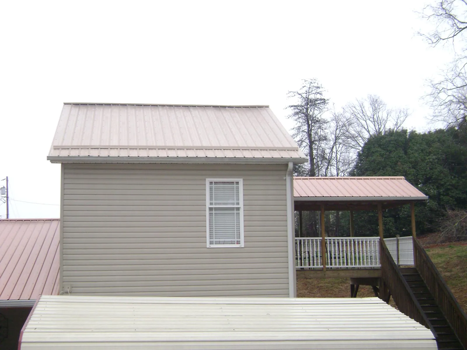 Tan metal roofs on a two story addition and attached porch, from a Roof Replacement job in Youngwood